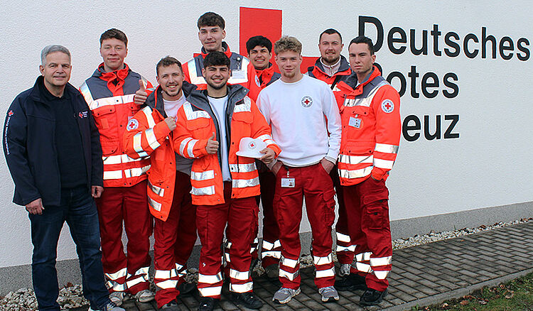 Gruppe von sieben Personen in roten und weißen Einsatzuniformen vor einer Wand mit dem Schriftzug Deutsches Rotes Kreuz