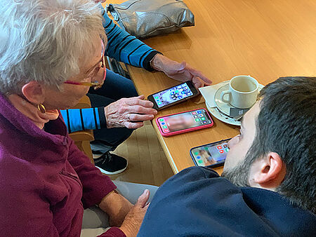 Junger Mann erklärt Senior den Umgang mit Smartphone.
